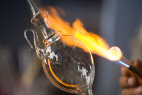 a hand holds a blow torch close to a blown glass figure to shape it