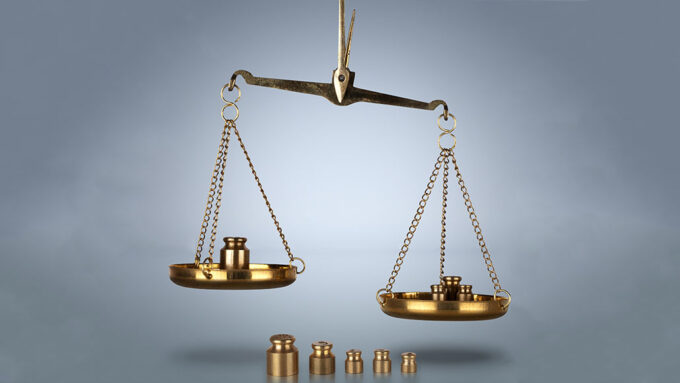 a picture of a brass metal balance scale, one each side are metal weights. One side is lower than the other side. There are also metal weights in front of the scale arranged from largest to smallest.