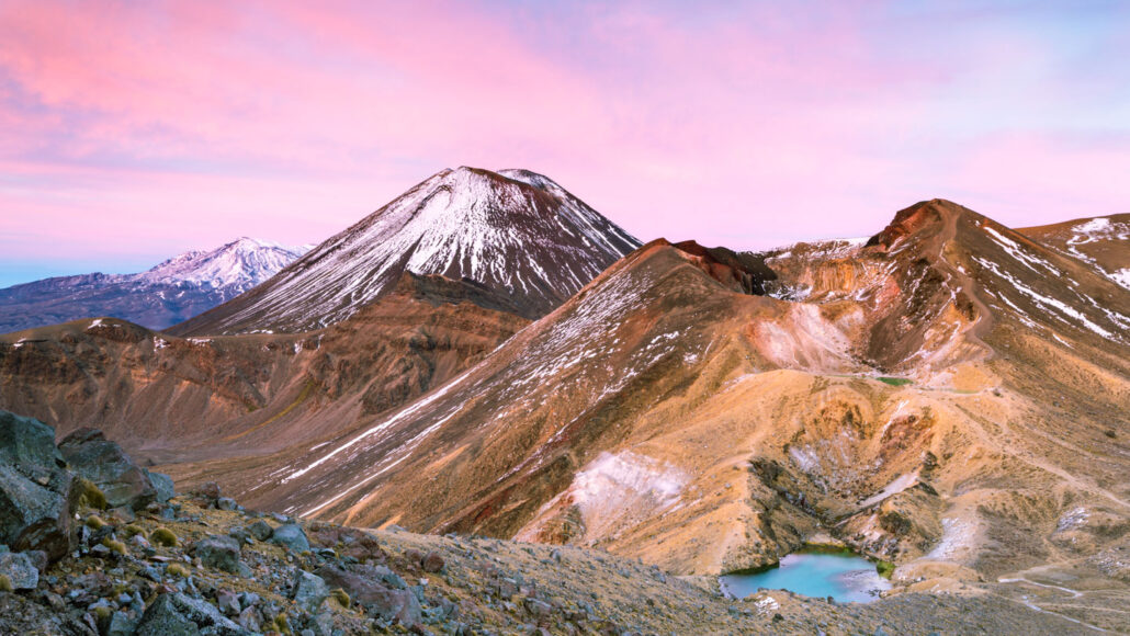 a pink sky at sunset over a mountain range dusted with snow at the top