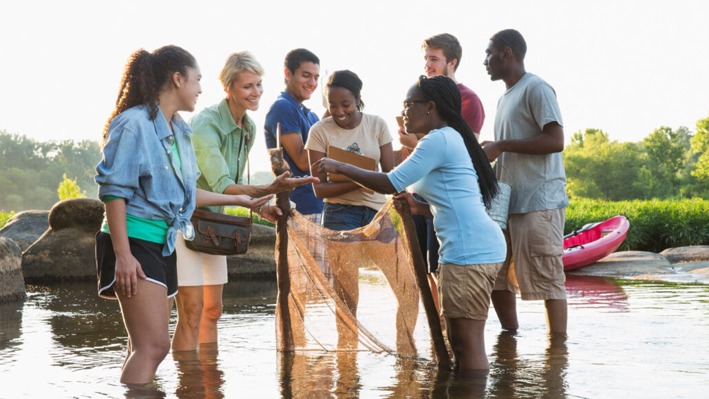 a group of young adults stand ankle-deep in river water
