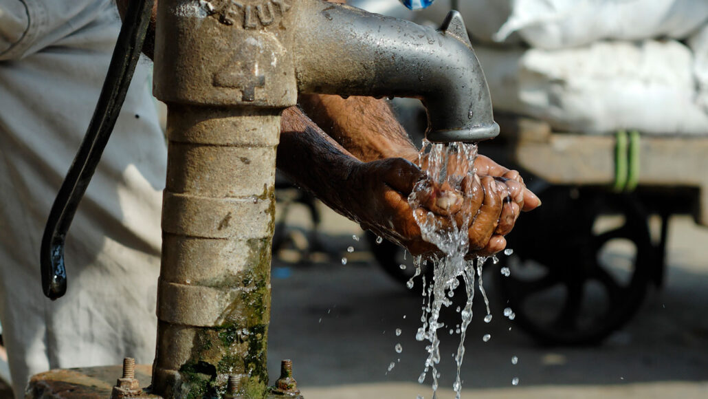 a pair of hands are cupped beneath the faucet of a borehole in the ground