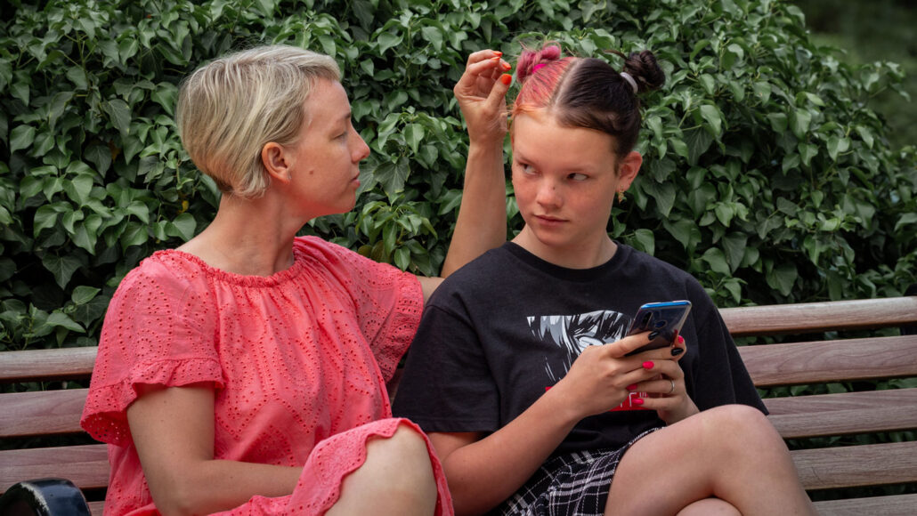 a mom looking at her daughter, who is looking annoyed while holding a phone