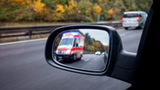 a closeup of a car side mirror shows an ambulance approaching from behind in a neighboring lane