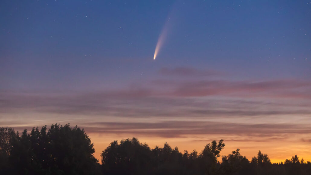 A photo of the sky at dusk with a comet streaking down across the middle of the image