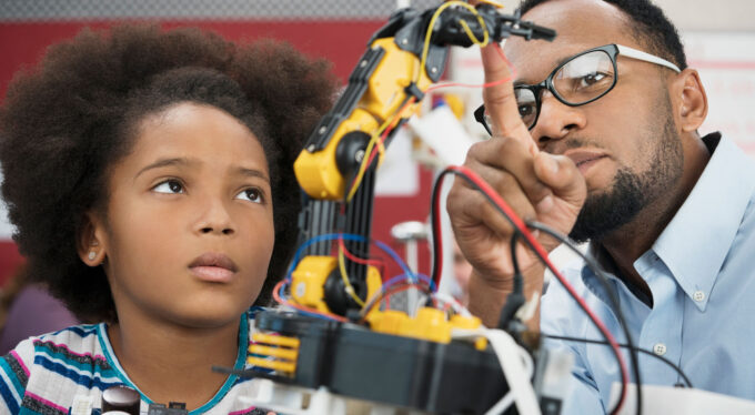 a man wearing glasses points out the components on robotic machinery to a tween girl