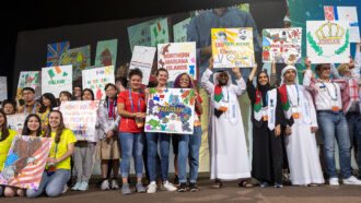 students from around the world stand on a stage at ISEF holding posters representing their countries