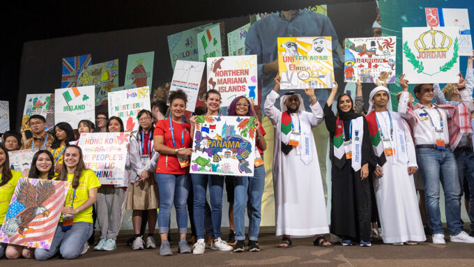 students from around the world stand on a stage at ISEF holding posters representing their countries