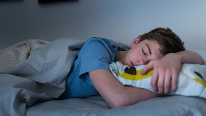 a teen boy snoozes in bed in a darkened room