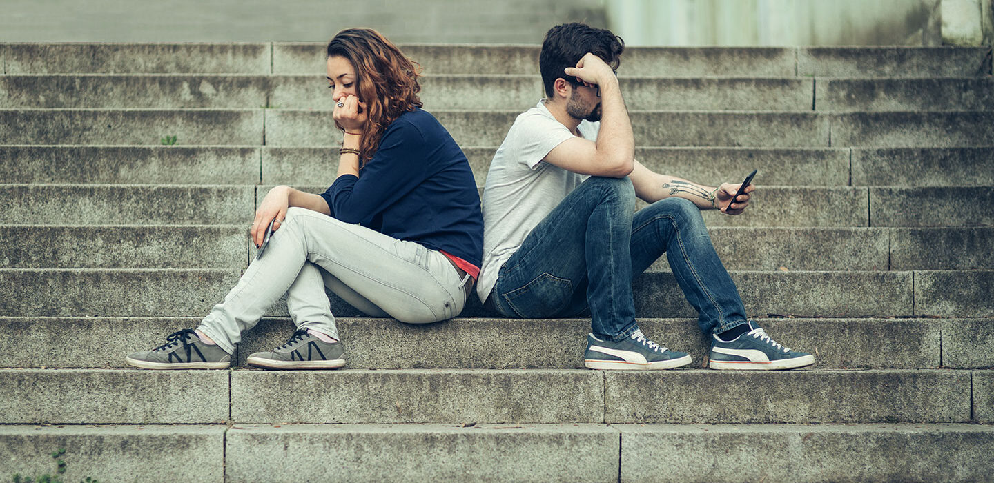 a young woman and a young man sitting on stairs back to back and looking upset