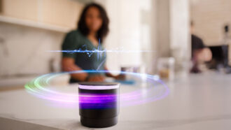 a woman looks at a smart speaker on a kitchen counter that appears to be listening