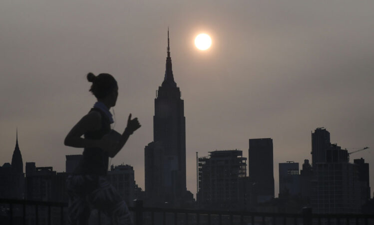 a photo of a hazy New York skyline and a woman jogging past in silhouette