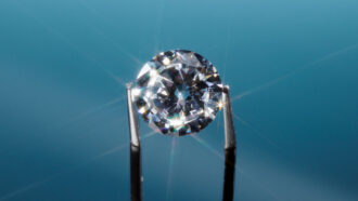 a pair of tweezers holds up a glittering diamond against a blue background