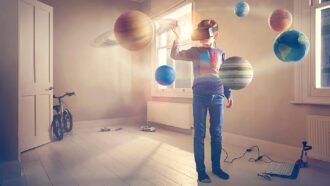 a boy wearing a VR headset stands in a bedroom where Earth, Jupiter and other planets float in the air