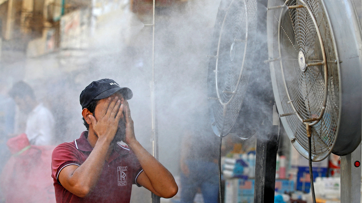 a man in a red shirt and a black cap standing in front of a misting fan