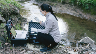 an Asian woman is testing water quality next to a stream