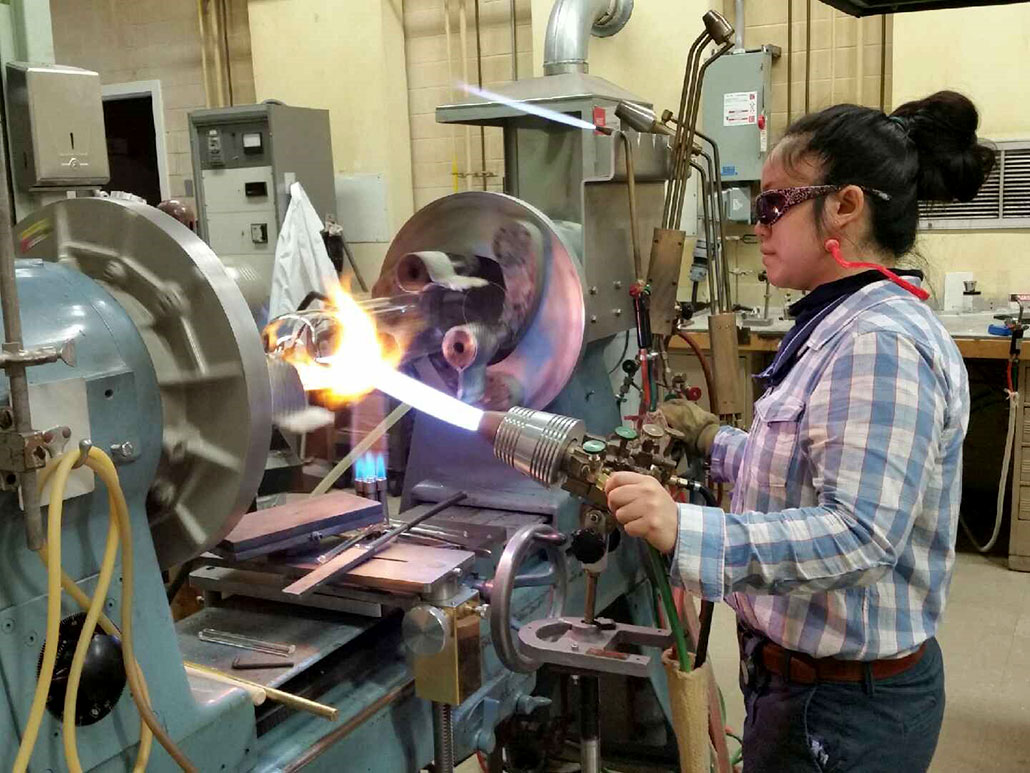 a photo showing Jo Wu using a lathe to rotate glass while she heats it
