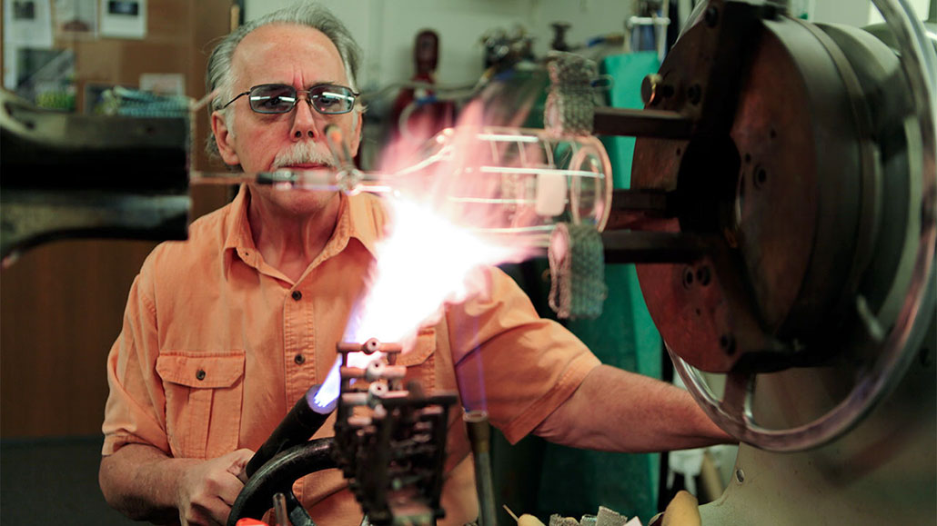 a photo of an older white man concentrating shaping a specialized flask  with fire