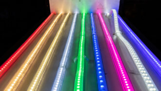 Nine strands of LED lights in different colors of the rainbow stretch out along a metal sheet against a black background