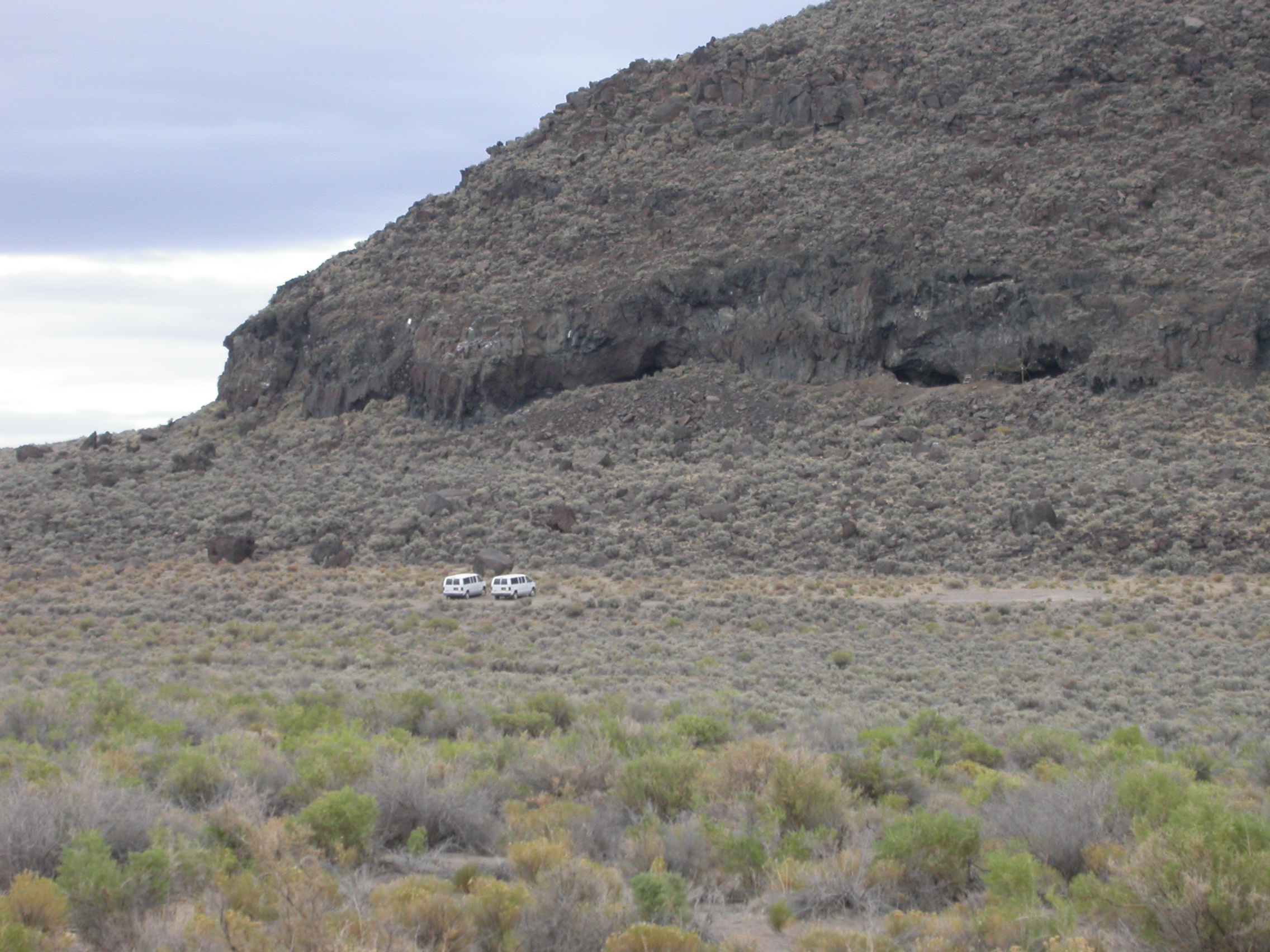 a sloping terrain with greenish brown shrubbery with two white vans parked at the base of a hill