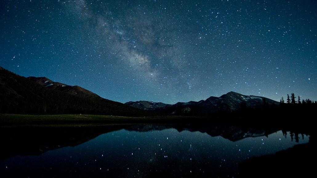 a photo of the Milky Way at night over a pond, there are mountains ringing the pond