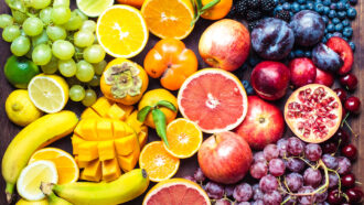 a mix of fruits including bananas, green and red grapes, oranges and grapefruits are bunched together on a table