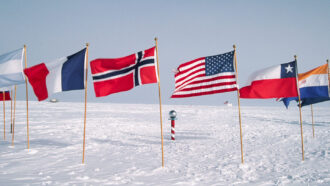 a circle of flags surround a small red and white pole poking out of the snow