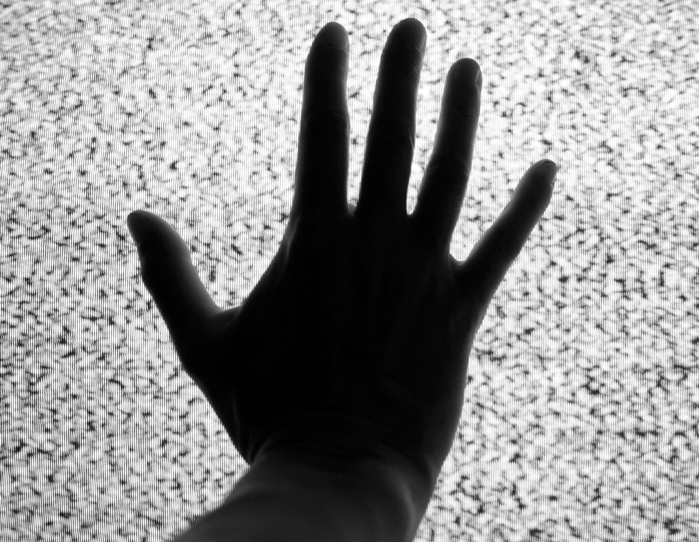 A silhouette of a hand presses against a staticky TV screen