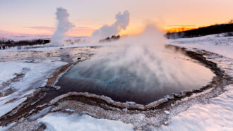steam rises off a pool of water surrounded by snow