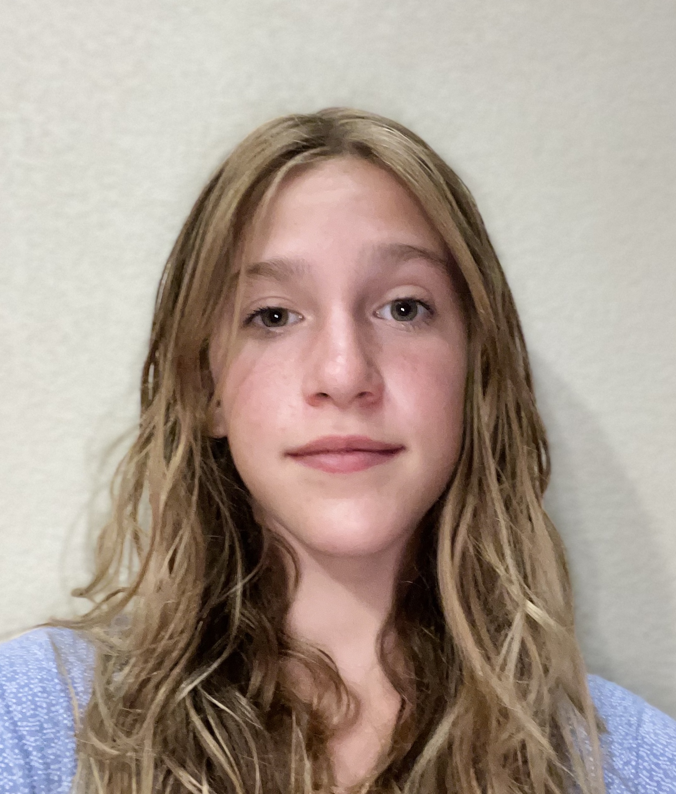 a blonde middle school girl stands in front of a white wall