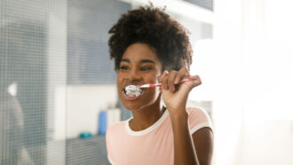 a Black teen with braces brushes her teeth