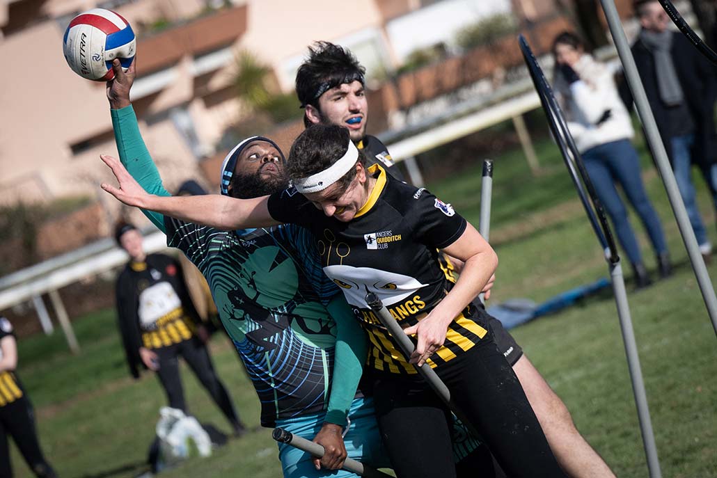 people playing Quidditch, one person is trying to throw a ball and two people are blocking him