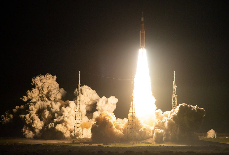 A night photo of the launch of the Space Launch System rocket with clouds of smoke and the bright path from the engines