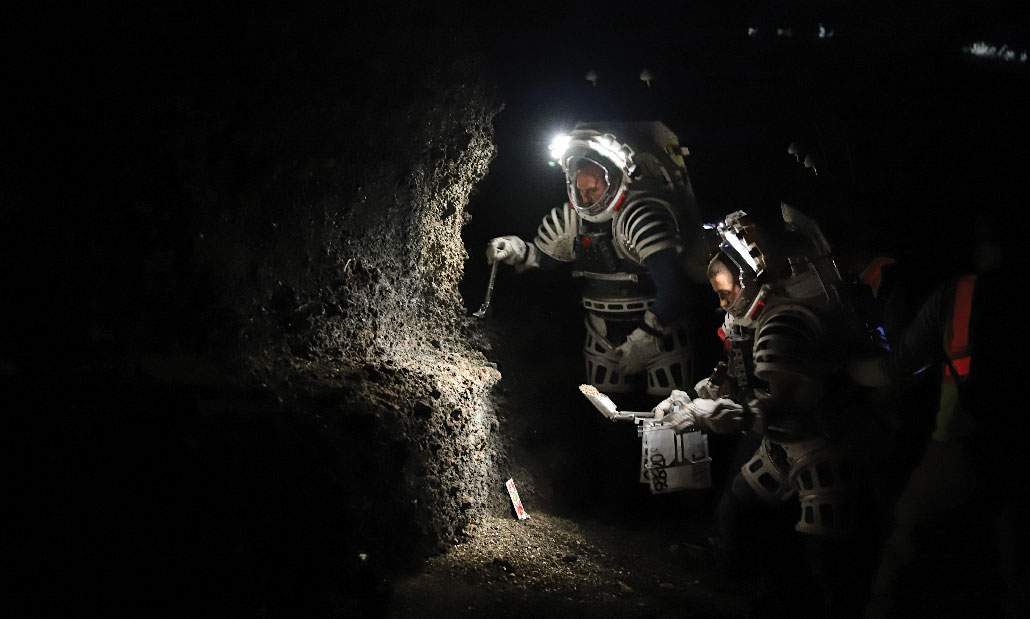 Engenheiros da NASA usam mochilas de caminhada espacial com faróis em um espaço escuro