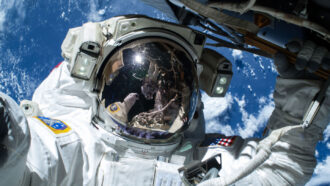 an astronaut wearing a space suit takes a selfie as they drift above the Earth