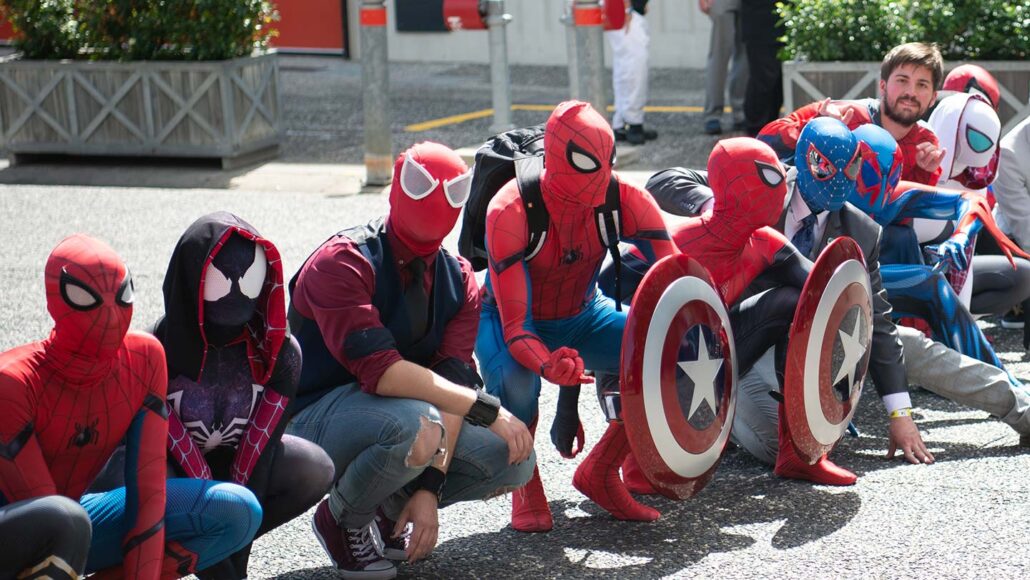 a line of people dressed in a variety of Spider-Man costumes are kneeling on pavement