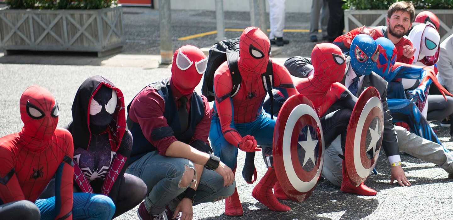 a line of people dressed in a variety of Spider-Man costumes are kneeling on pavement