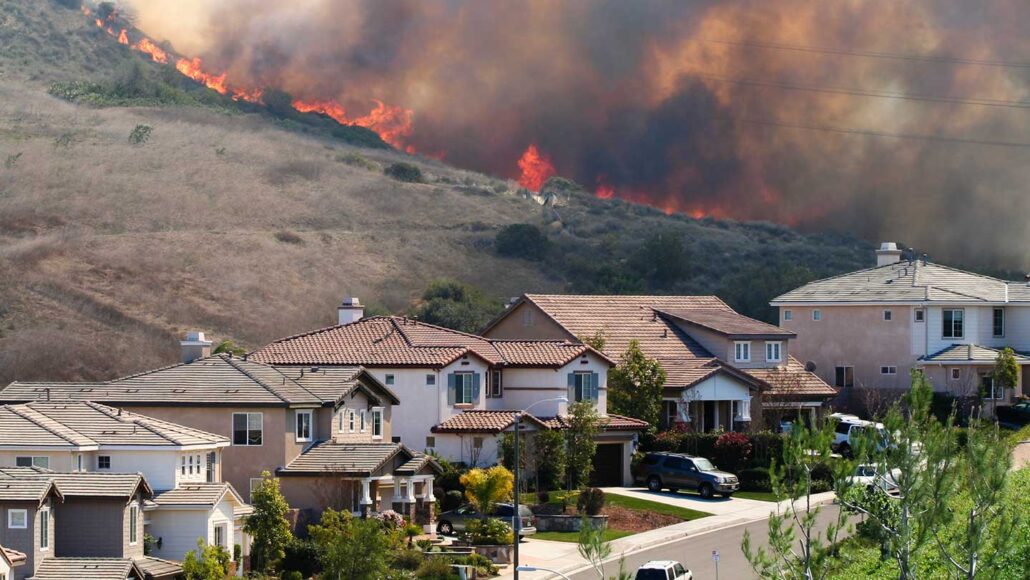 a photo of a ridge on fire behind a nehigborhood. The air is black with smoke.