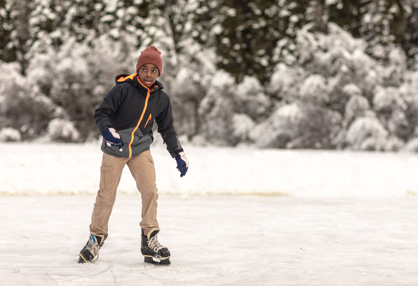 A boy wearing winter clothes skates across the frozen surface of a pond
