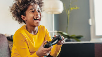 a photo of a young black girl with a short curly hairstly playing a video game and laughing
