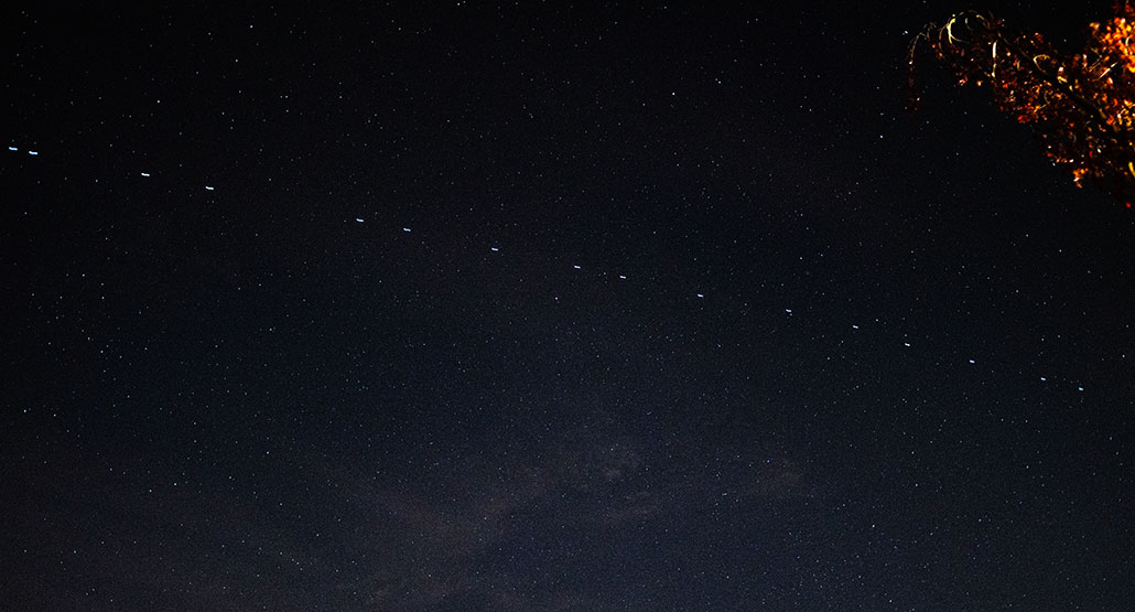 a photo of a starry night sky with a bright line of white dashes (LEO satellites) overhead