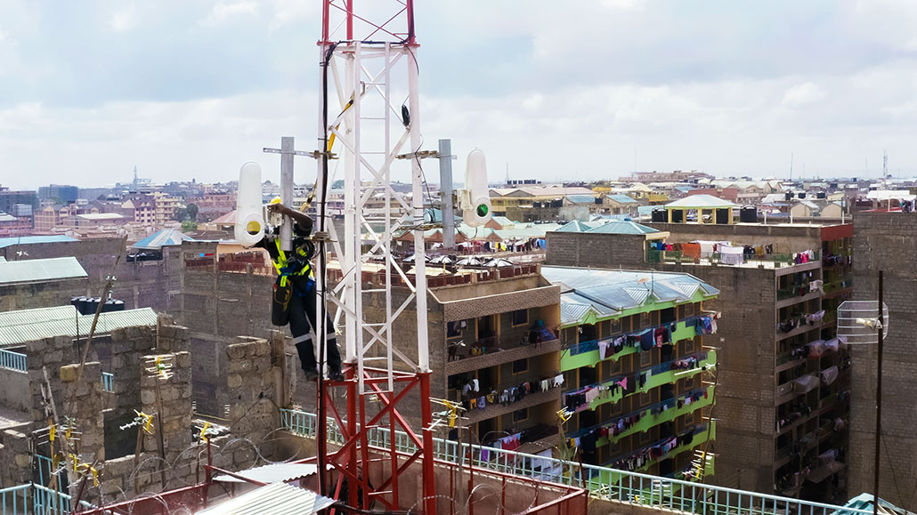 a photo of a person installing a WOC terminal on a tower atop a building in the city  Will the internet soon reach the one-third of people without it?   1030 Internet for all WOC terminal