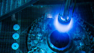 a photo of reactor core submerged in water during refueling, a blue glow can be seen at the end of the core (a metallic cylinder)