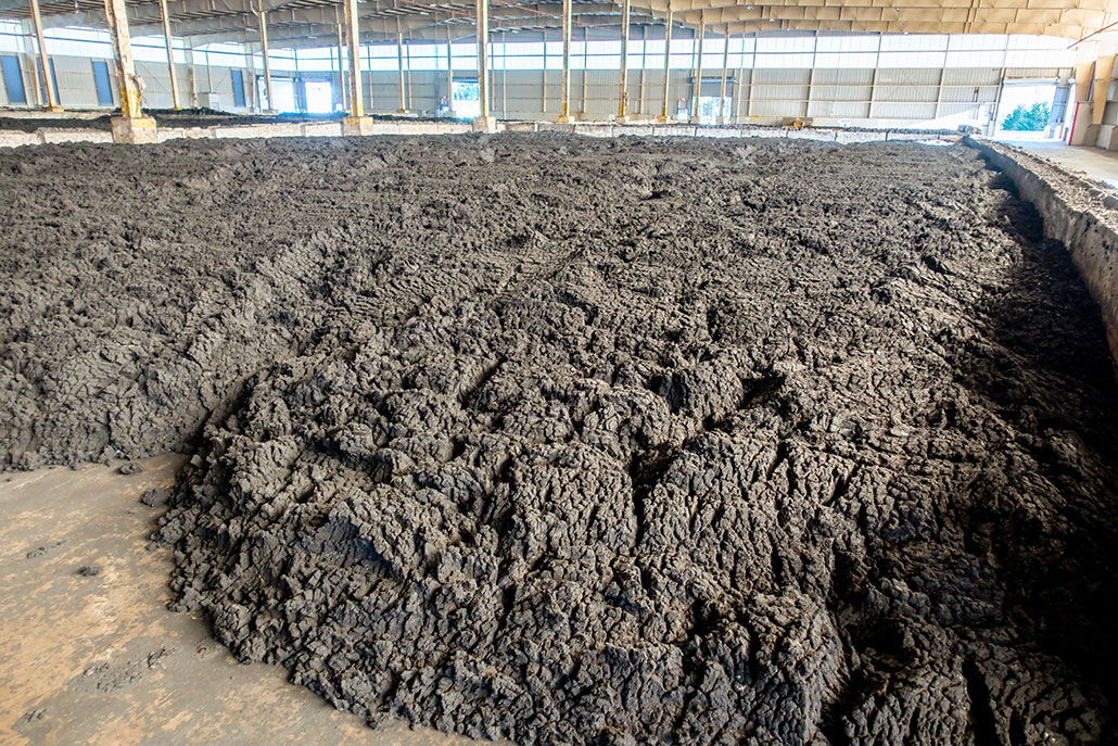 A large structure encloses a cement covered pit. Inside the pit are mounds of gray-brown dirt material, biosolids, that are being stored for future use. 