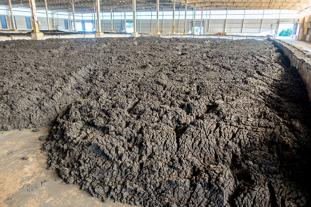 A large structure encloses a cement covered pit. Inside the pit are mounds of gray-brown dirt material, biosolids, that are being stored for future use.