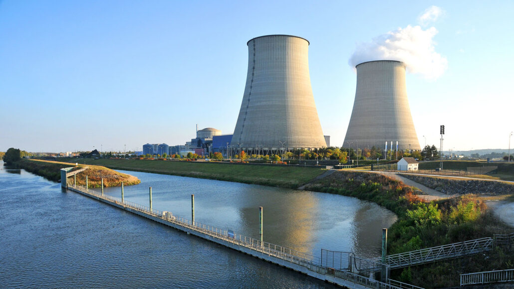 a nuclear power plant with two concrete smoke stacks stands beside a body of water
