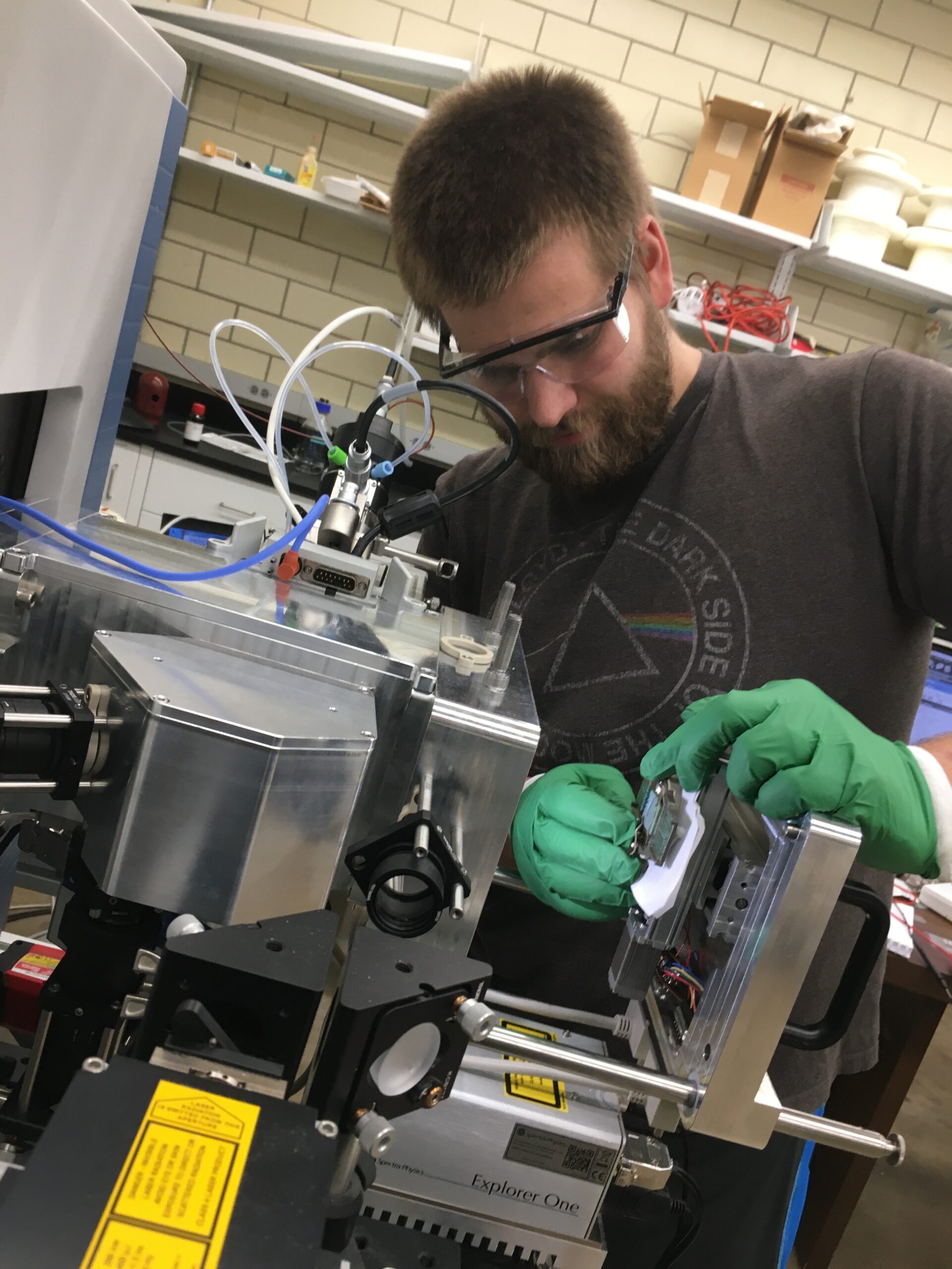 a young man wearing goggles and gloves works on a piece of machinery at a lab bench