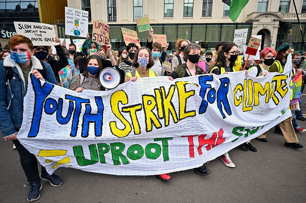 a photo of masked students marching in the street with a long banner reading 'Youth Strike for Climate', people behind the banner are holding up various protest signs