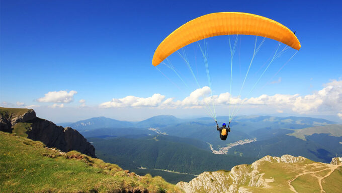 a photo of a person using a parachute to glide over gorgeous mountain terrain on a sunny day
