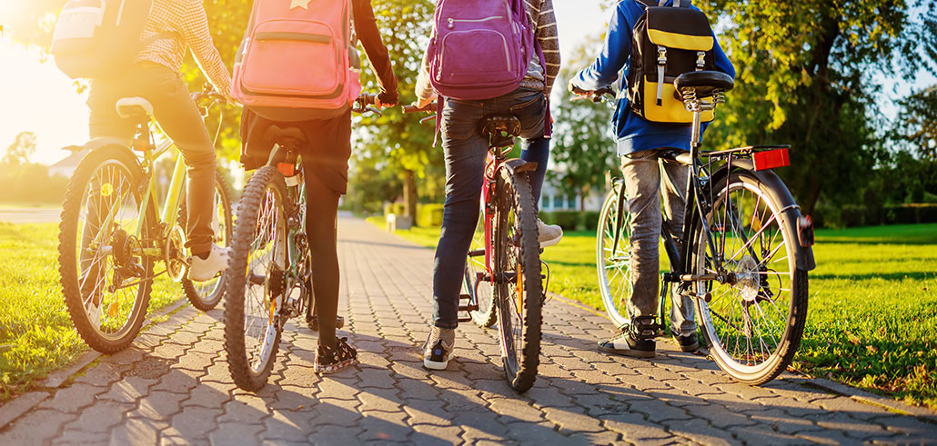 a photo of four kids on bikes, they are stopped on a paved sidewalk facing away from the viewer