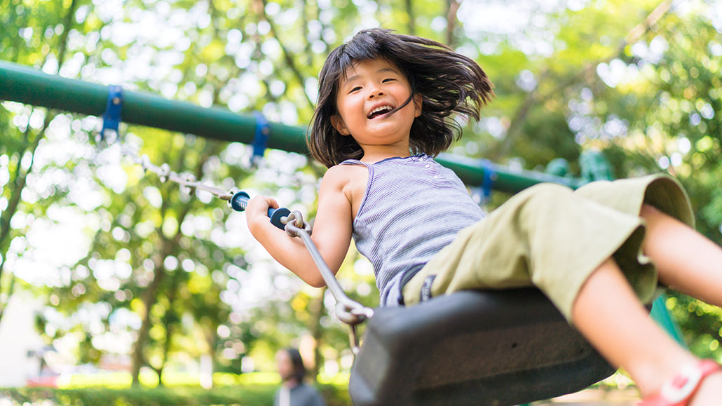 A Girl looks happy swinging on a swingset surrounded by trees